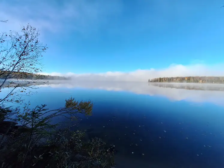 Fog lifting off a still blue lake in the Almaguin Highlands