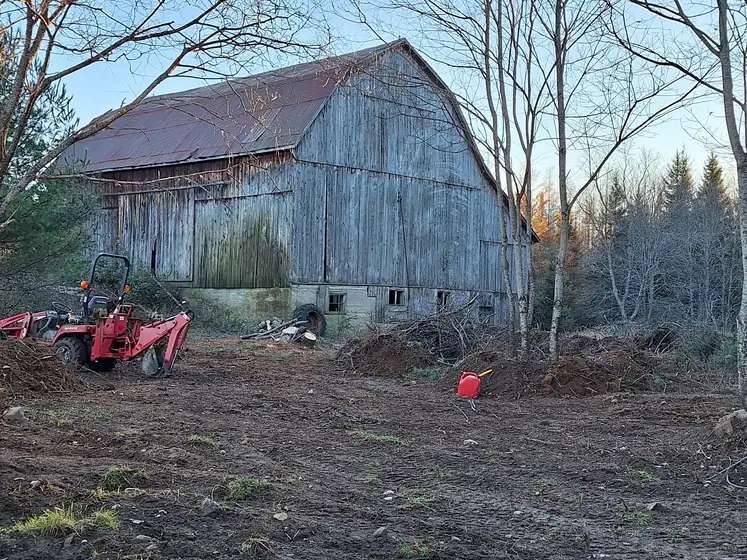 Grey gambrel barn with a red tractor parked beside it