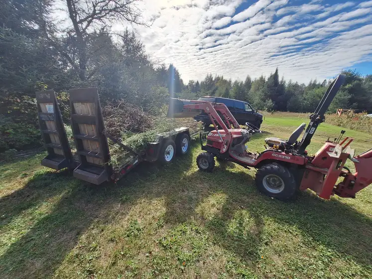 Equipment trailer with ramps beside a red tractor with a backhoe