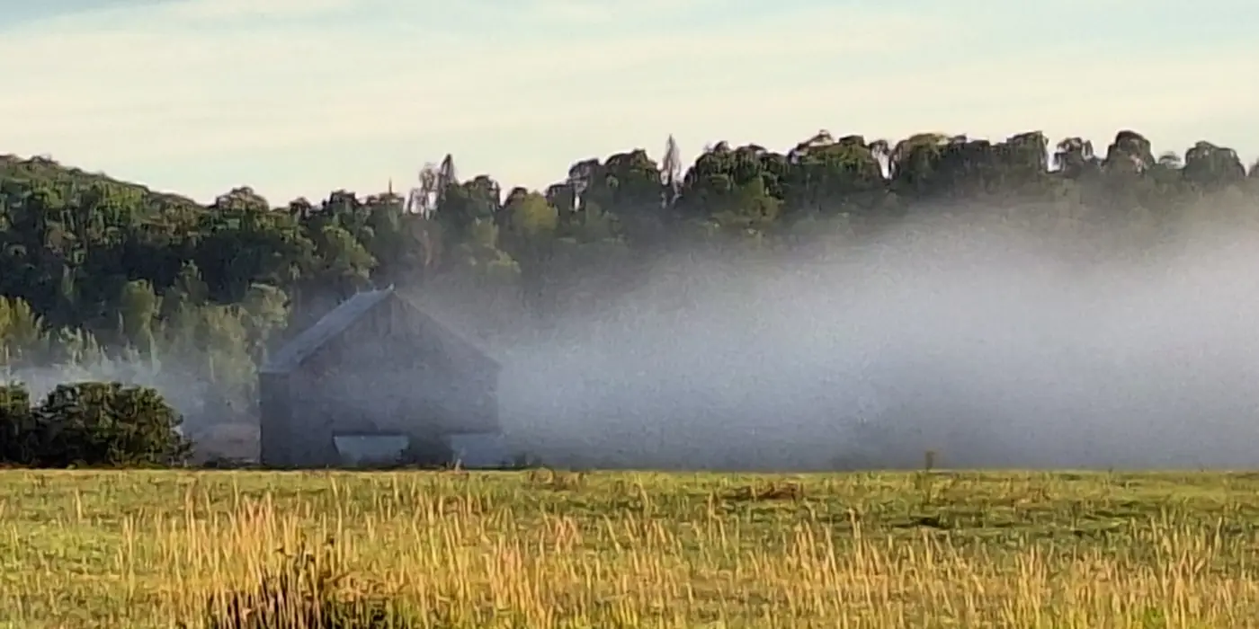 Morning fog lifting over a hay field and an old grey barn near South River, Ontario