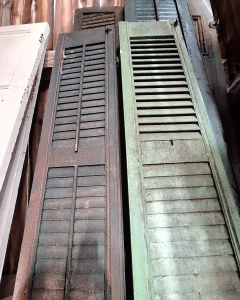 Old green and brown wooden shutters leaning against a barn wall, saved for reuse