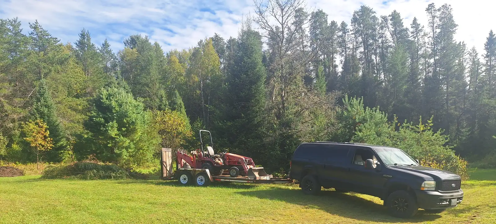 The Ravens Ridge truck and equipment trailer parked on a field in South River, with spruce and pine behind